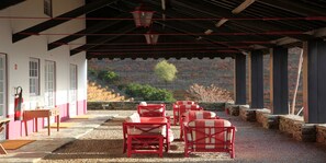 Un espace extérieur abrité avec des chaises rouges et une table, un extincteur, et une vue sur le feuillage automnal.