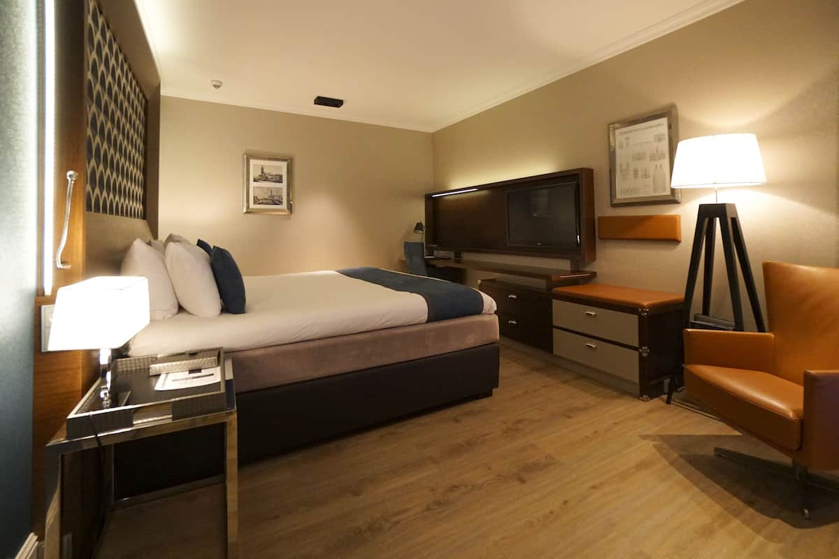 Une chambre d’hôtel avec un lit, un bureau, une chaise, une télévision et une lampe.