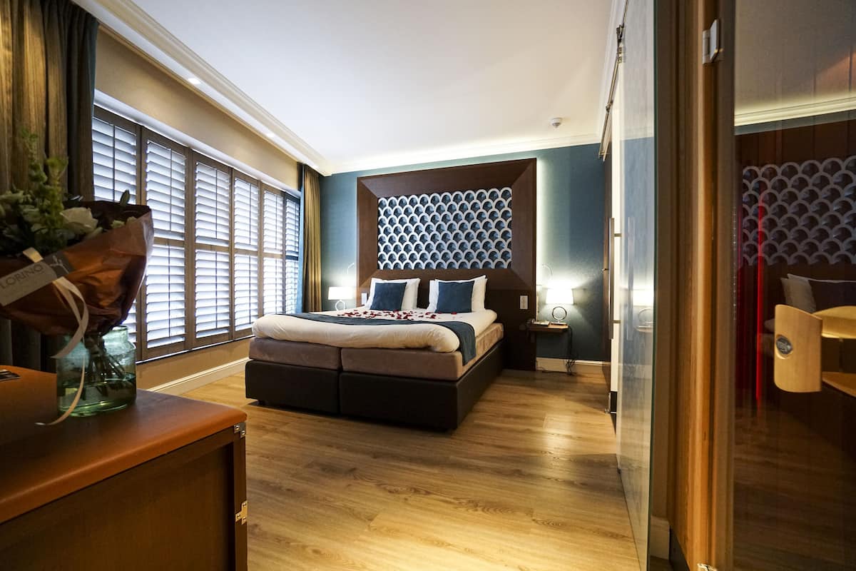 Une chambre moderne avec un grand lit, un plancher en bois, un panneau décoratif au mur et une vue sur l’extérieur grâce à de grandes fenêtres.
