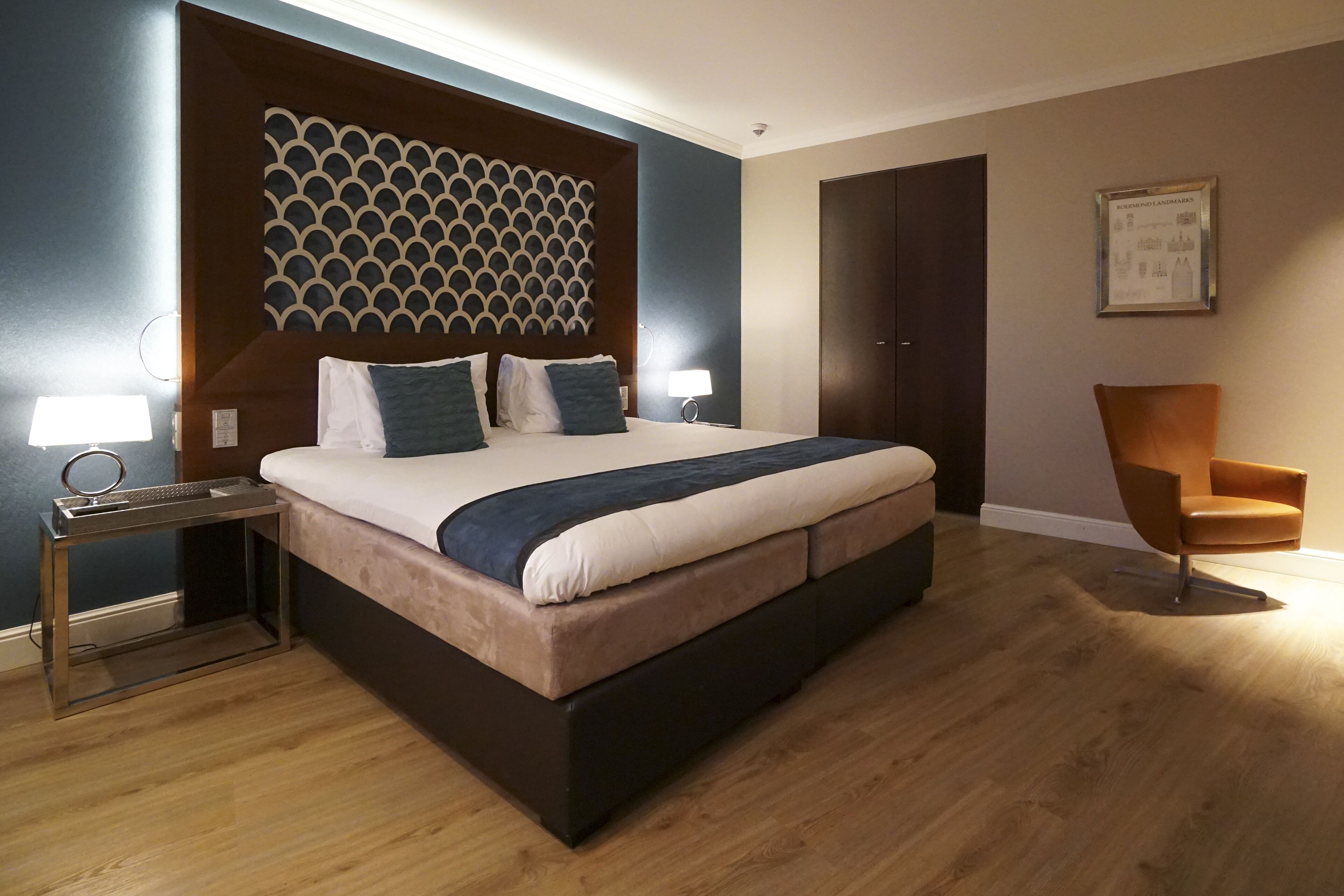 Una habitación de hotel moderna con una cama grande, una mesita de noche, una silla y un panel decorativo en la pared.