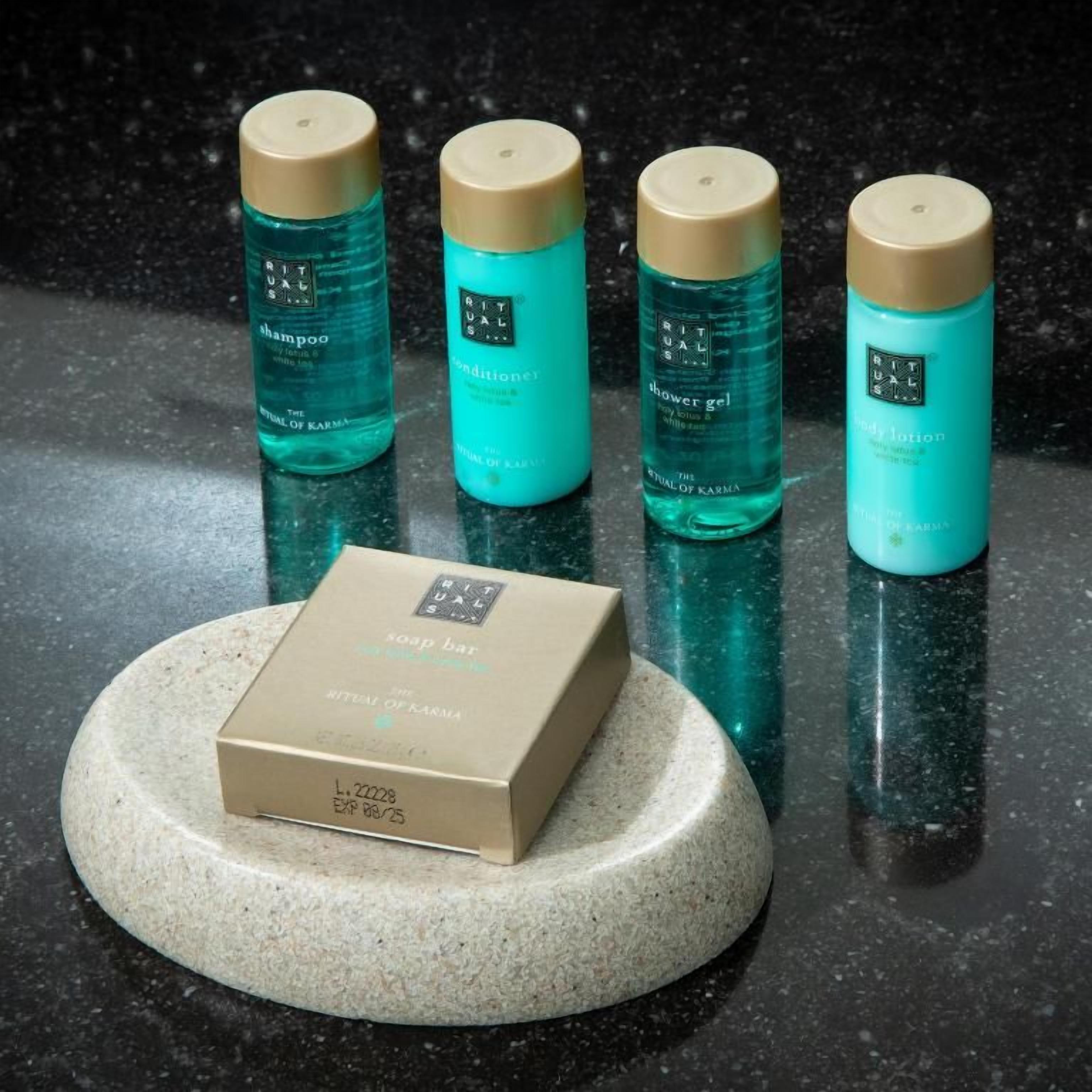 Cuatro botellas de productos Ritual de Karma sobre una superficie reflectante, junto con la caja de una barra de jabón.