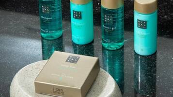 Cuatro botellas de productos Ritual de Karma sobre una superficie reflectante, junto con la caja de una barra de jabón.