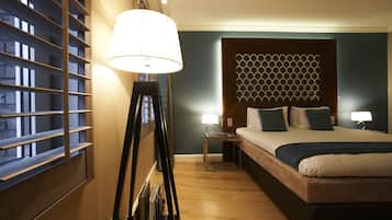 Een hotelkamer met een bed, nachtlampjes, een raam met zonwering en een wandlamp.
