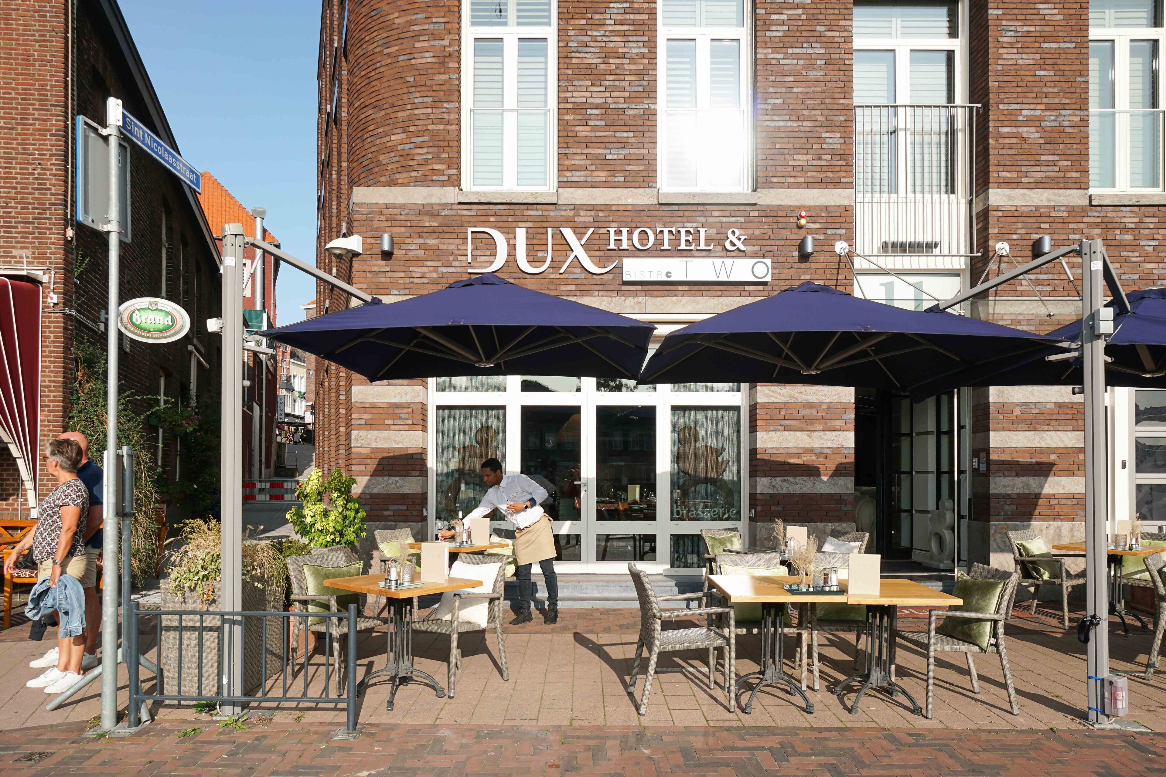 A brick building with the sign "Dux Hotel & Restaurant Two" and outdoor seating with umbrellas.