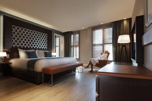 Una habitación de hotel con una cama grande, un banco, un escritorio y un televisor.