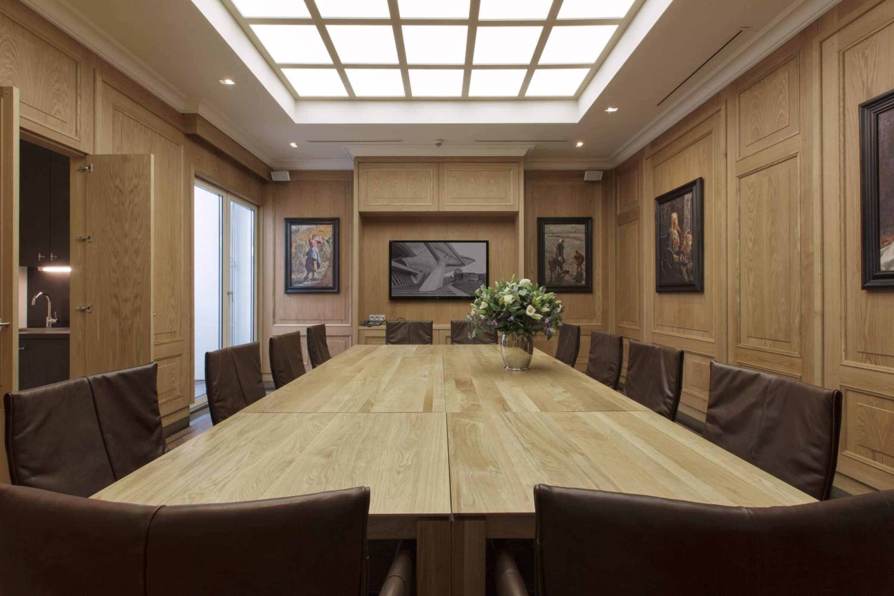 Ein Konferenzraum mit langem Tisch, braunen Ledersesseln, Holzwandverkleidung und gerahmten Kunstwerken.