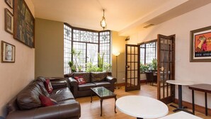 A cozy living room with a leather sofa, a glass coffee table, and a round table. There are large windows with a view of the outdoors. - Hotel Strand Continental - Hostel (London)