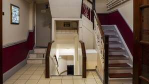 A staircase with a fire exit sign, a door with a security camera, and a tiled floor. - Hotel Strand Continental - Hostel (London)
