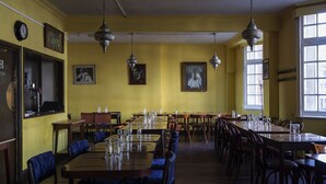 A dining area with multiple tables and chairs, yellow walls, and hanging light fixtures. - Hotel Strand Continental - Hostel (London)
