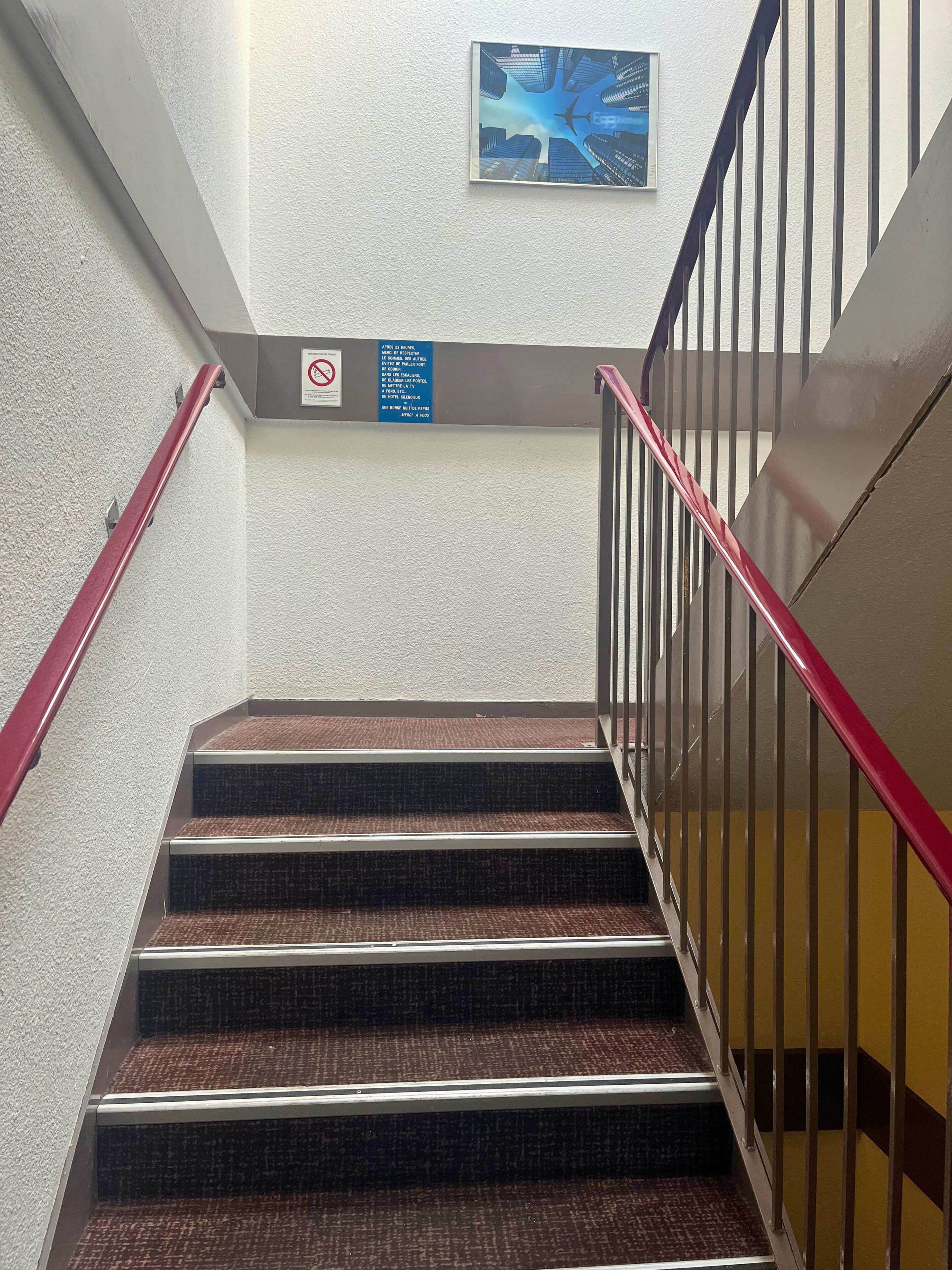 A staircase with red handrails, carpeted steps, and a blue sign on the wall.