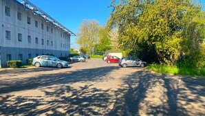 Un parcheggio con diverse auto, un edificio dotato di pannelli solari e alberi con chioma verde.