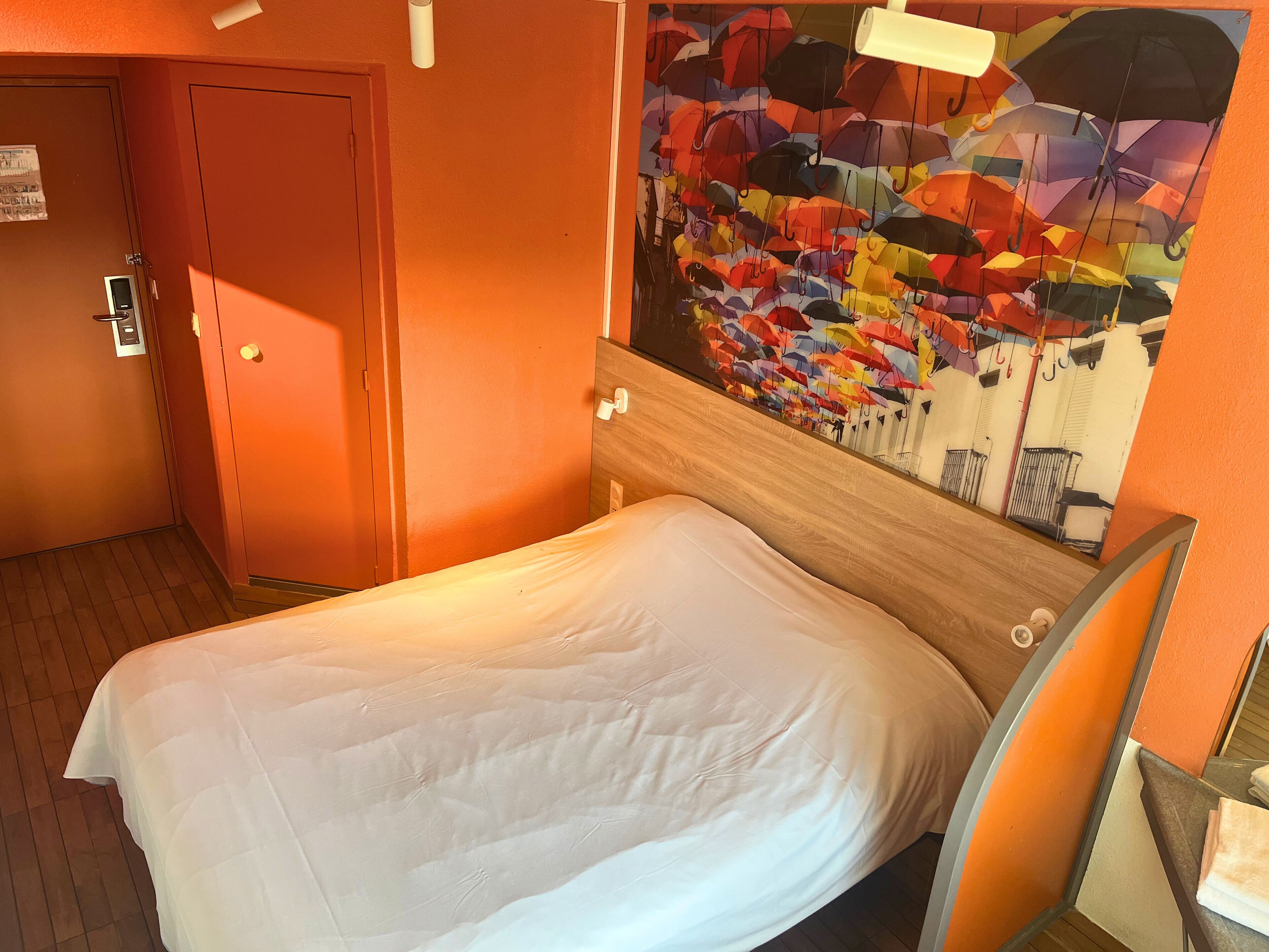 Habitación de hotel con cama, una puerta y pared con un mural de un paraguas colorido.