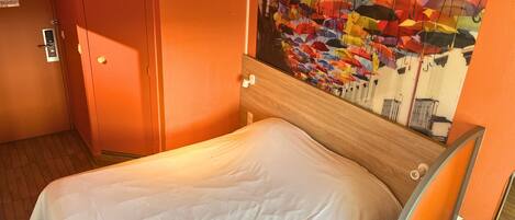 Habitación de hotel con cama, una puerta y pared con un mural de un paraguas colorido.