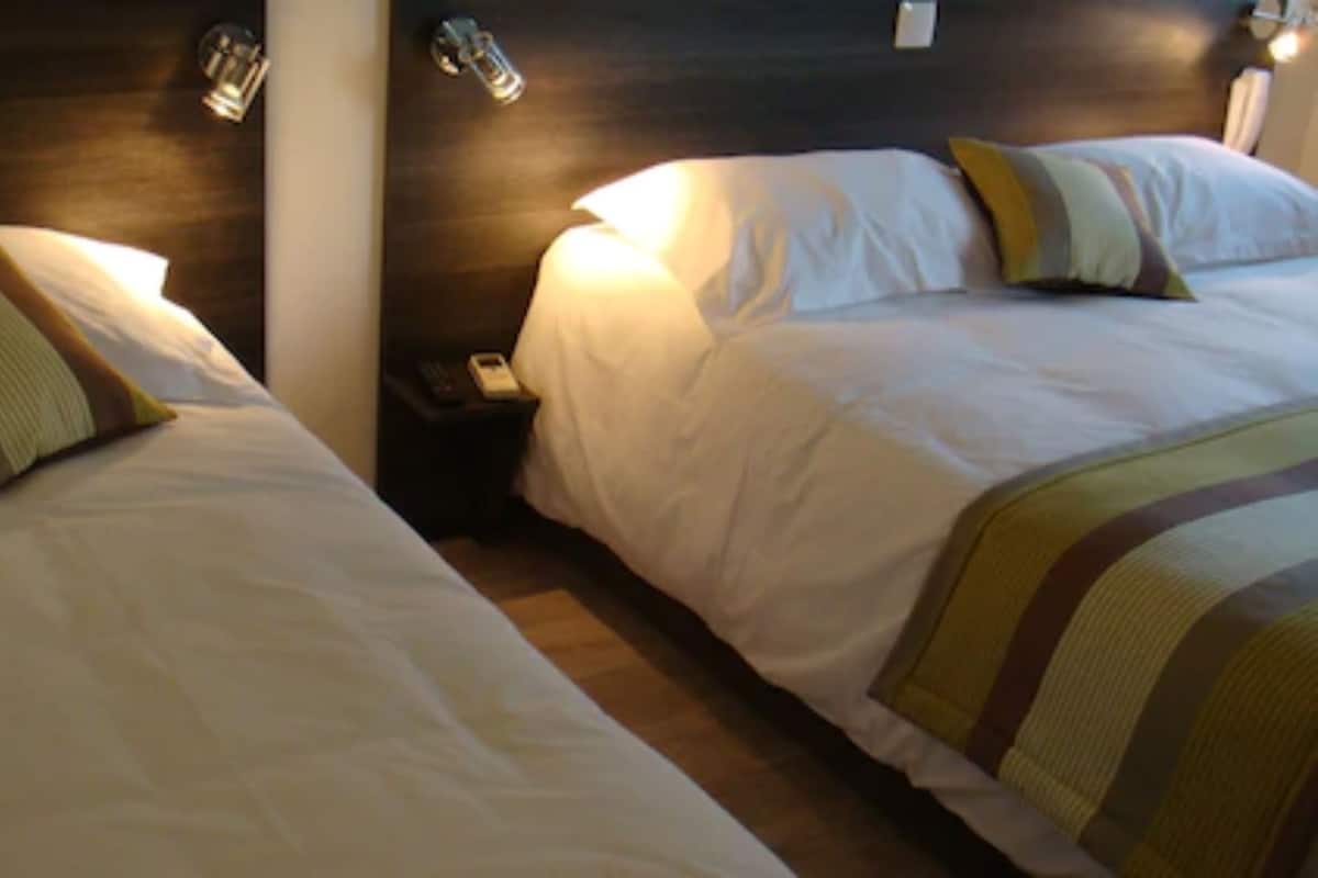 Deux lits avec du linge de lit blanc et des couvertures à rayures, une table de chevet avec un téléphone et des lampes fixées au mur.