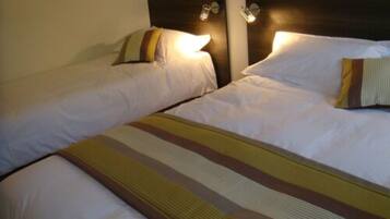 A hotel room with two single beds, each with a pillow and a headboard with a light fixture.