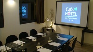 Una sala de conferencias con una larga mesa, sillas, una pantalla de proyector mostrando 'Côte Hôtel' y un ventanal con cortinas.