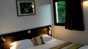 Una cama bien hecha con un edredón a rayas, una lámpara de noche y un cuadro en la pared.