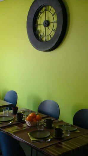 A dining area with a round clock and a table set for a meal, surrounded by a green wall and comfortable seating.
