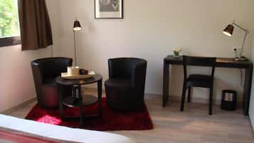 A hotel room with a bed, two black chairs, a small round table, a desk with a chair, a red rug, a framed picture on the wall, and two floor lamps.