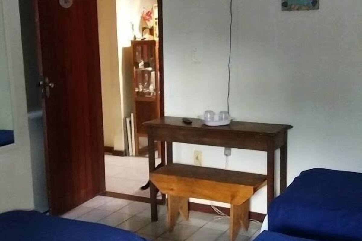 Una habitación con dos camas, un banco de madera, una mesita, un televisor montado en la pared y una puerta que da a otra estancia.