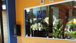 A room with two wooden lounge chairs, a large window with framed pictures, and a stone-tiled floor. - Pousada Barcarola (Búzios)