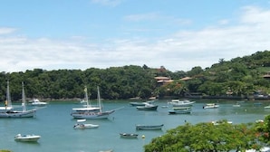 A coastal area with several boats docked near a hillside with houses. - Pousada Barcarola (Búzios)