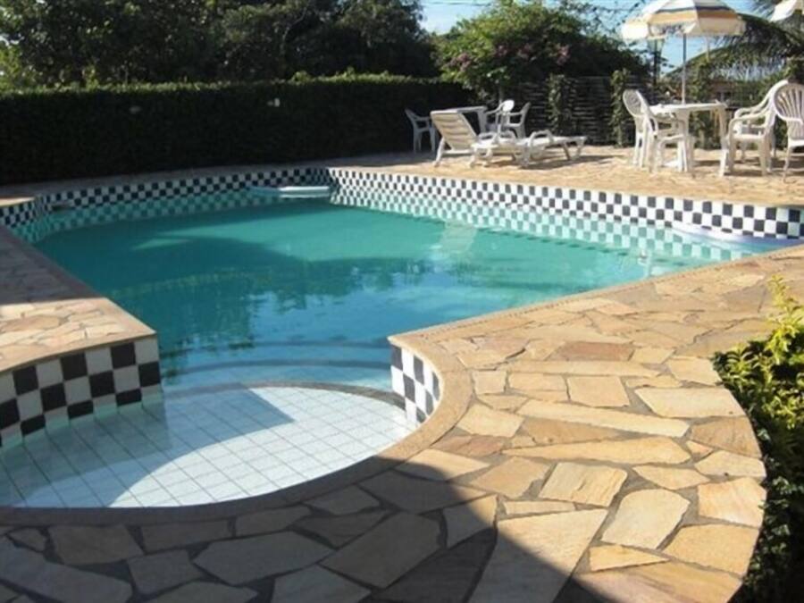 A swimming pool with a checkered edge, surrounded by stone tiles and white plastic chairs.