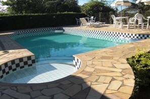 A swimming pool with a checkered edge, surrounded by stone tiles and white plastic chairs. - Pousada Barcarola (Búzios)