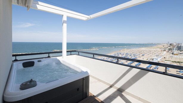 A balcony with a hot tub overlooking a beach with umbrellas and a pier. - Baia (Rimini)