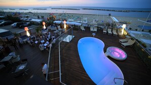 A rooftop bar with a pool, lounge chairs, and a view of the beach and sea. - Baia (Rimini)