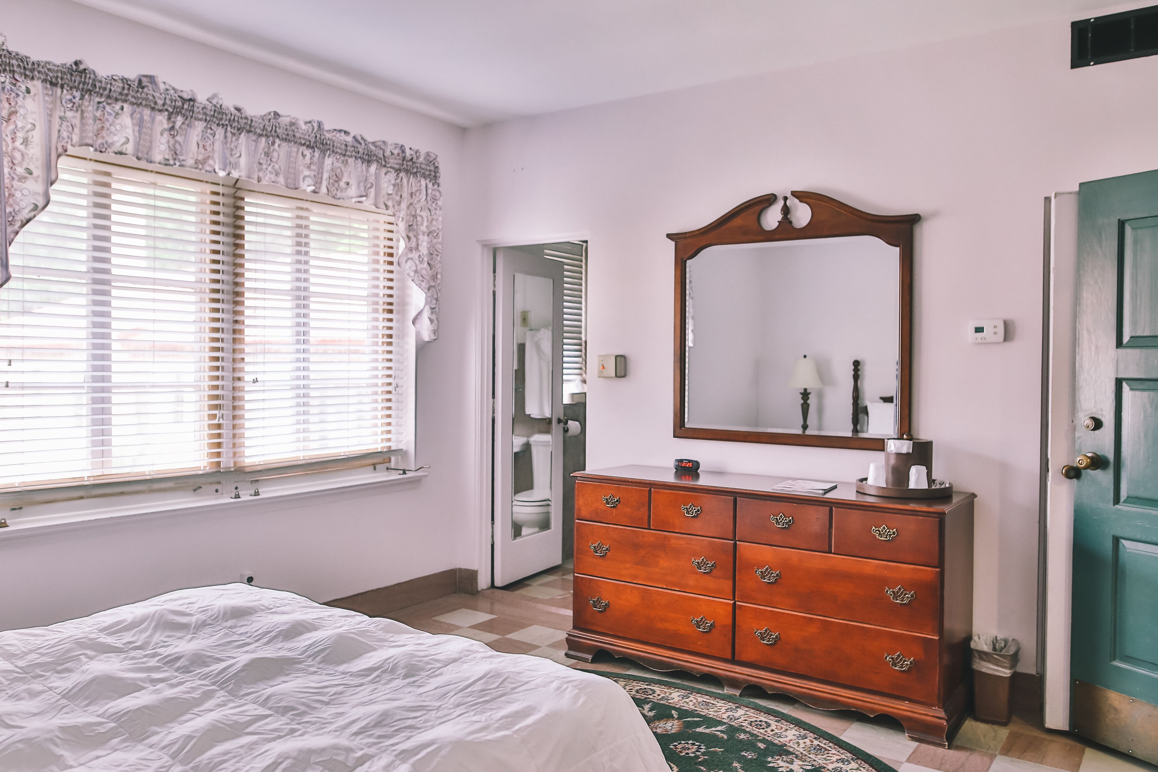 A bedroom with a bed, dresser, mirror, and window with blinds.