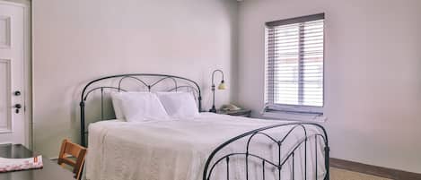 Un dormitorio con una cama, una mesita de noche, una lámpara, una ventana con persianas y una puerta.