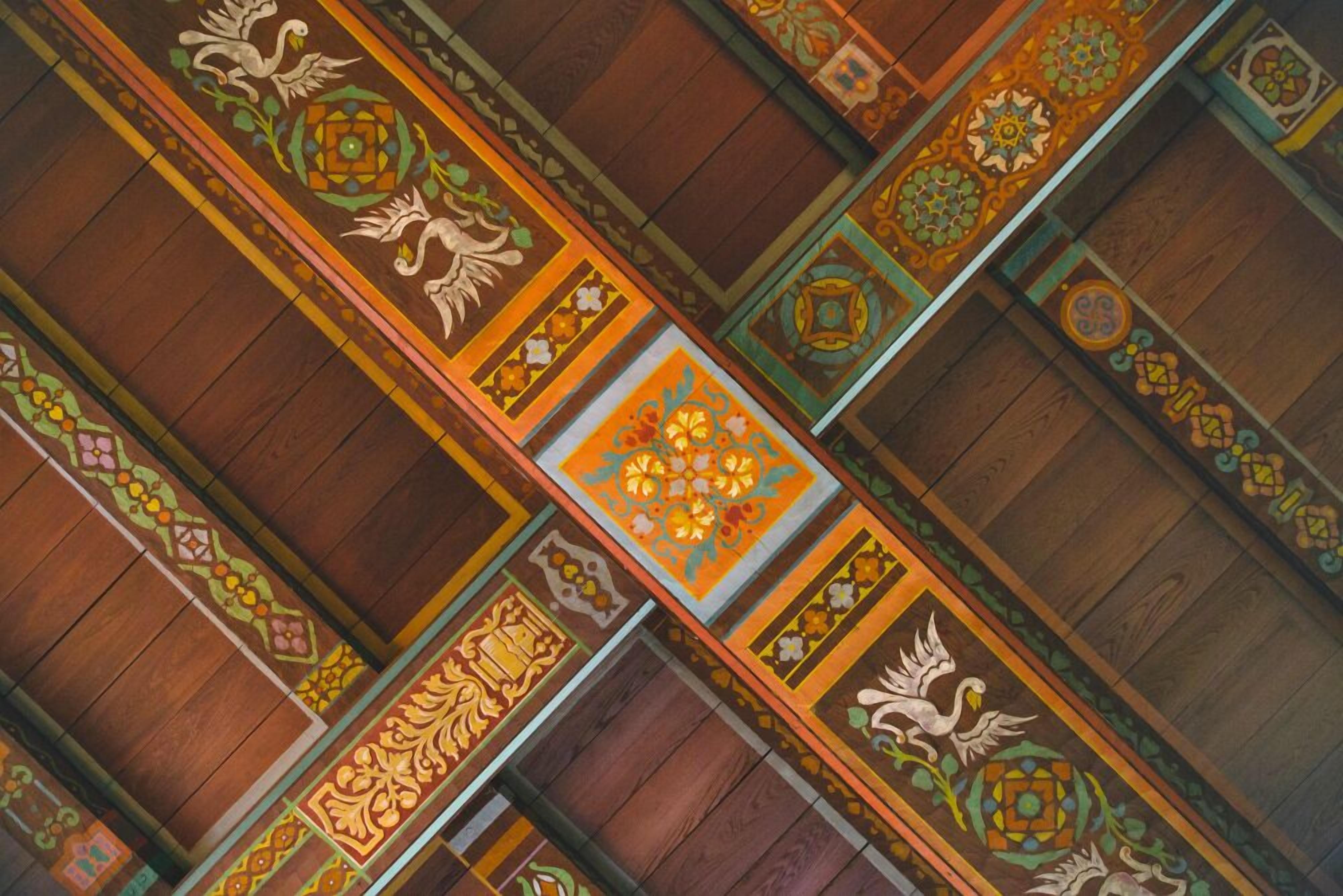Un plafond richement décoré, orné de motifs géométriques et floraux complexes, de poutres en bois et d’un motif carré central.