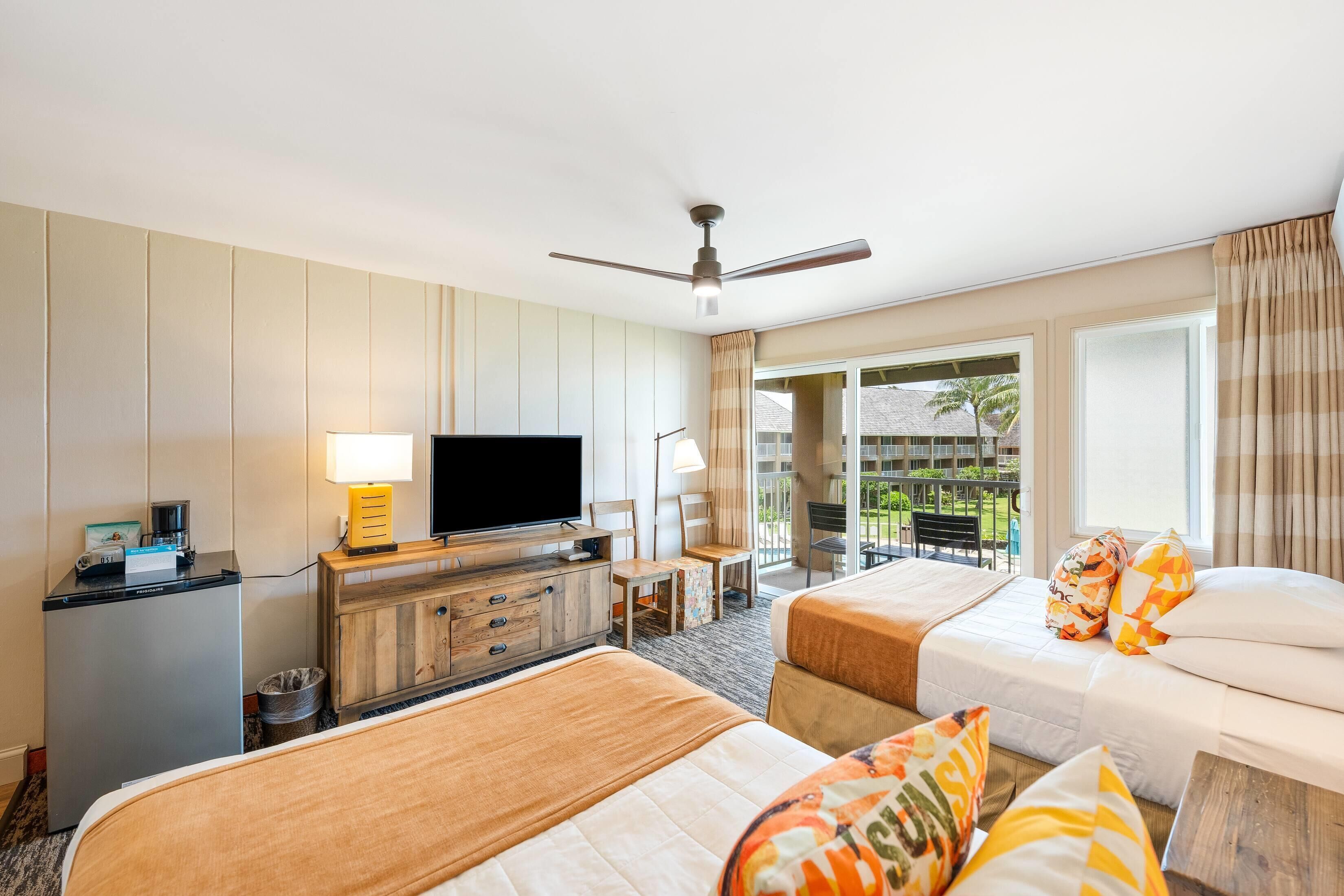 Habitación de hotel con dos camas, televisión, escritorio y vistas al exterior.