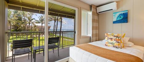 A hotel room with a balcony, a bed with a white comforter, and a painting of a wave.