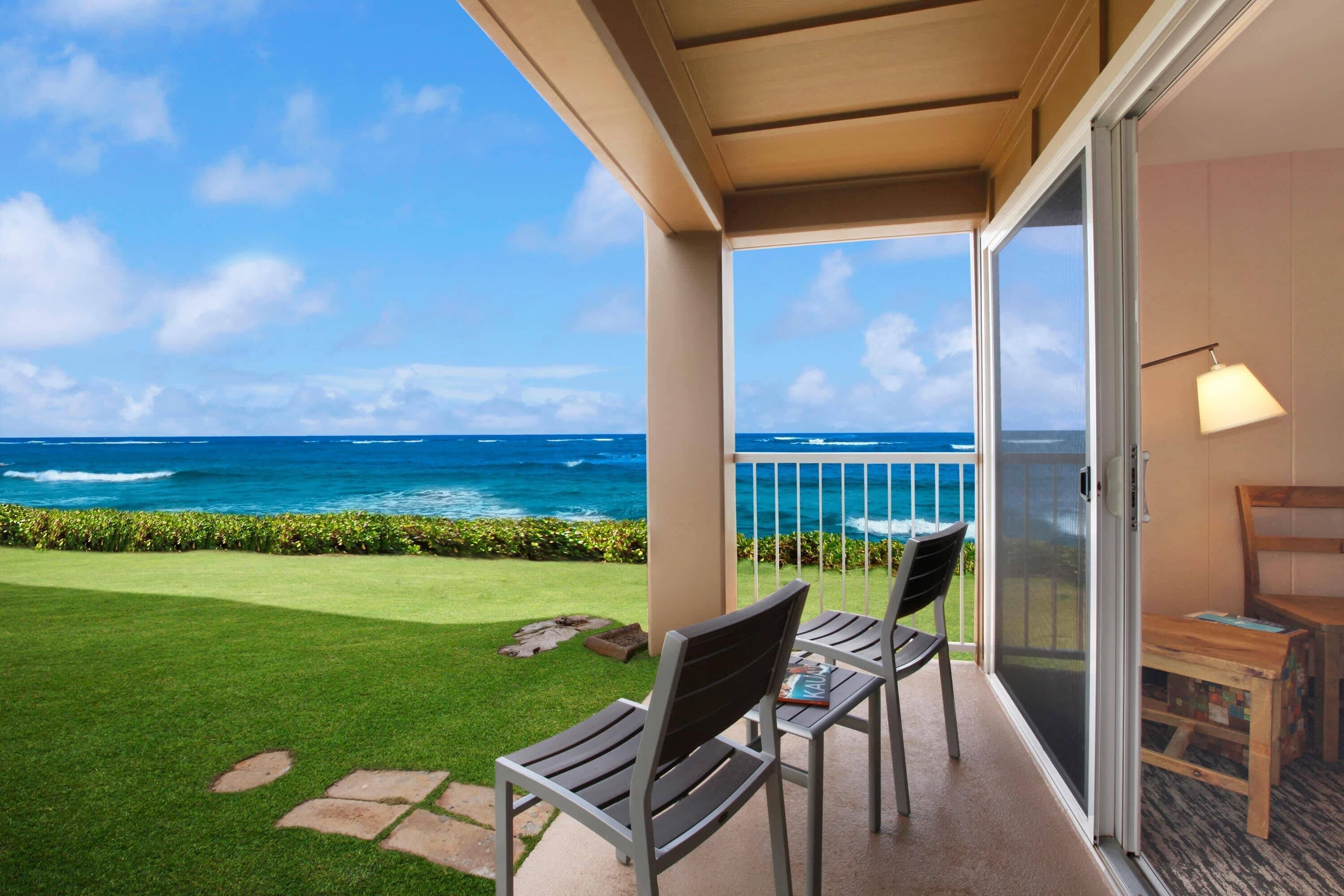 A balcony with a view of the ocean, two chairs, a small table, and a lamp.