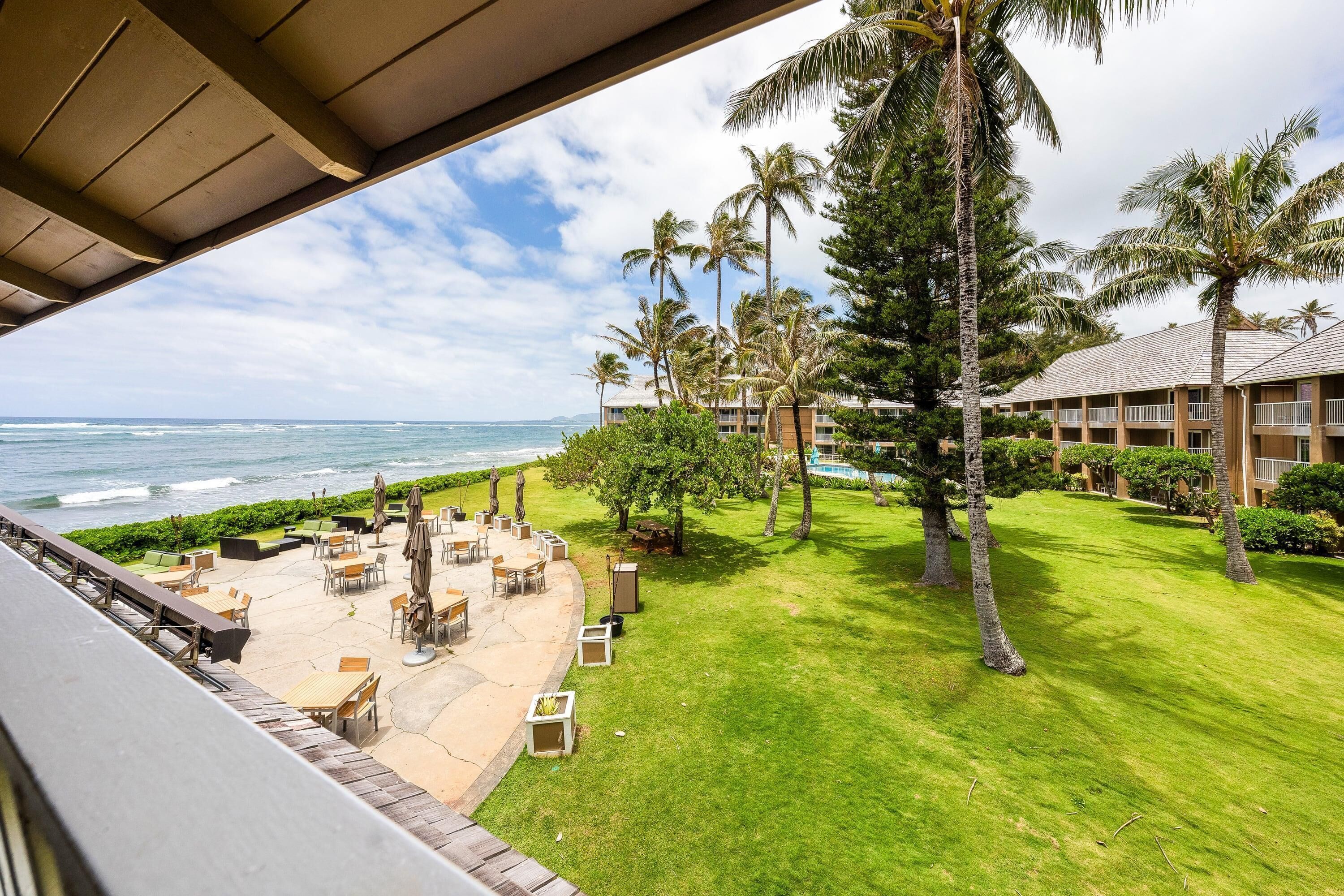 A hotel with a view of the ocean, outdoor seating, and palm trees.