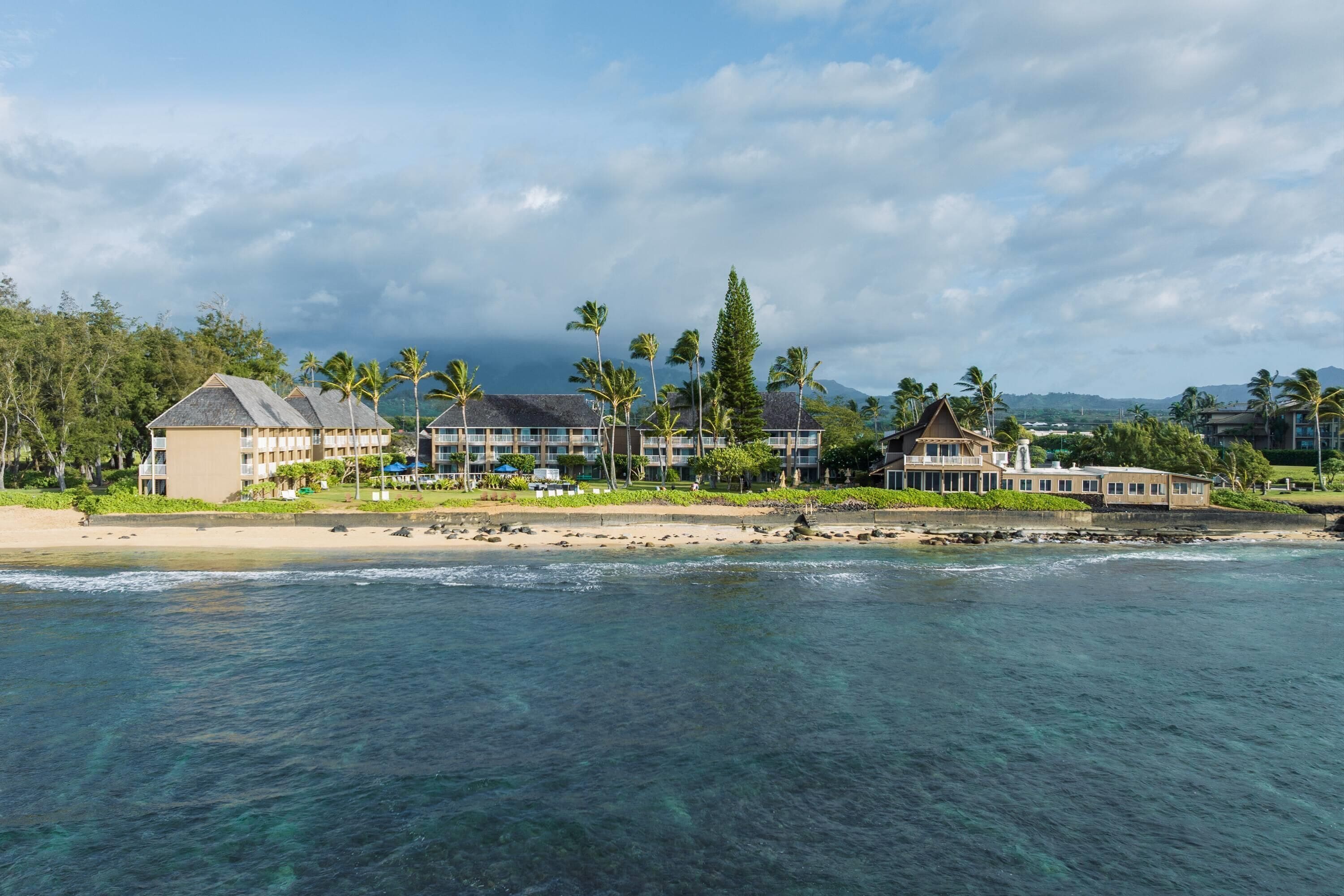 A beachfront hotel with multiple buildings, a sandy beach, and palm trees.
