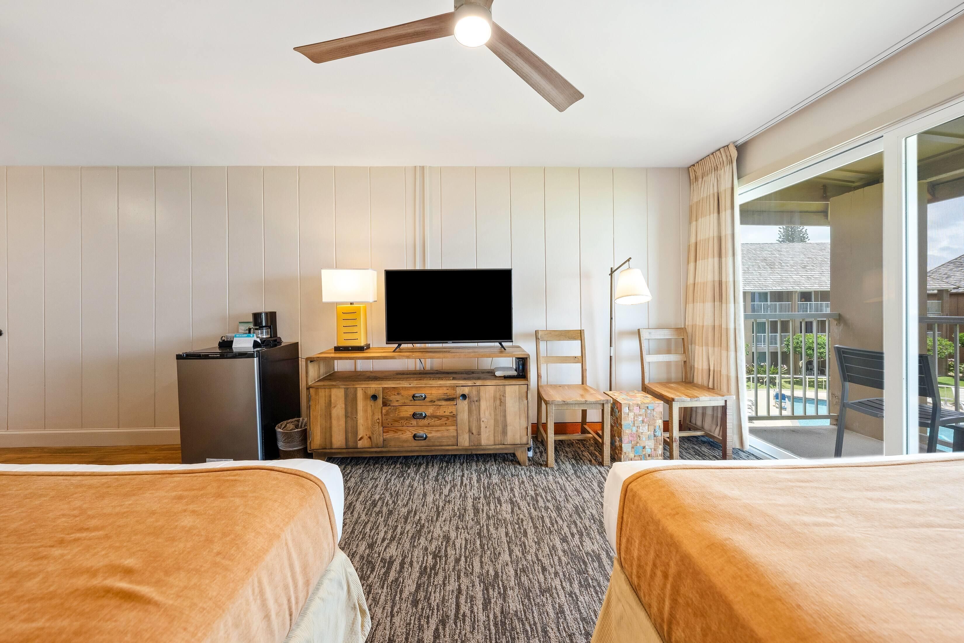 A hotel room with two beds, a TV, a wooden dresser, and a balcony with a view.