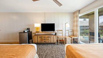 A hotel room with two beds, a TV, a wooden dresser, and a balcony with a view.
