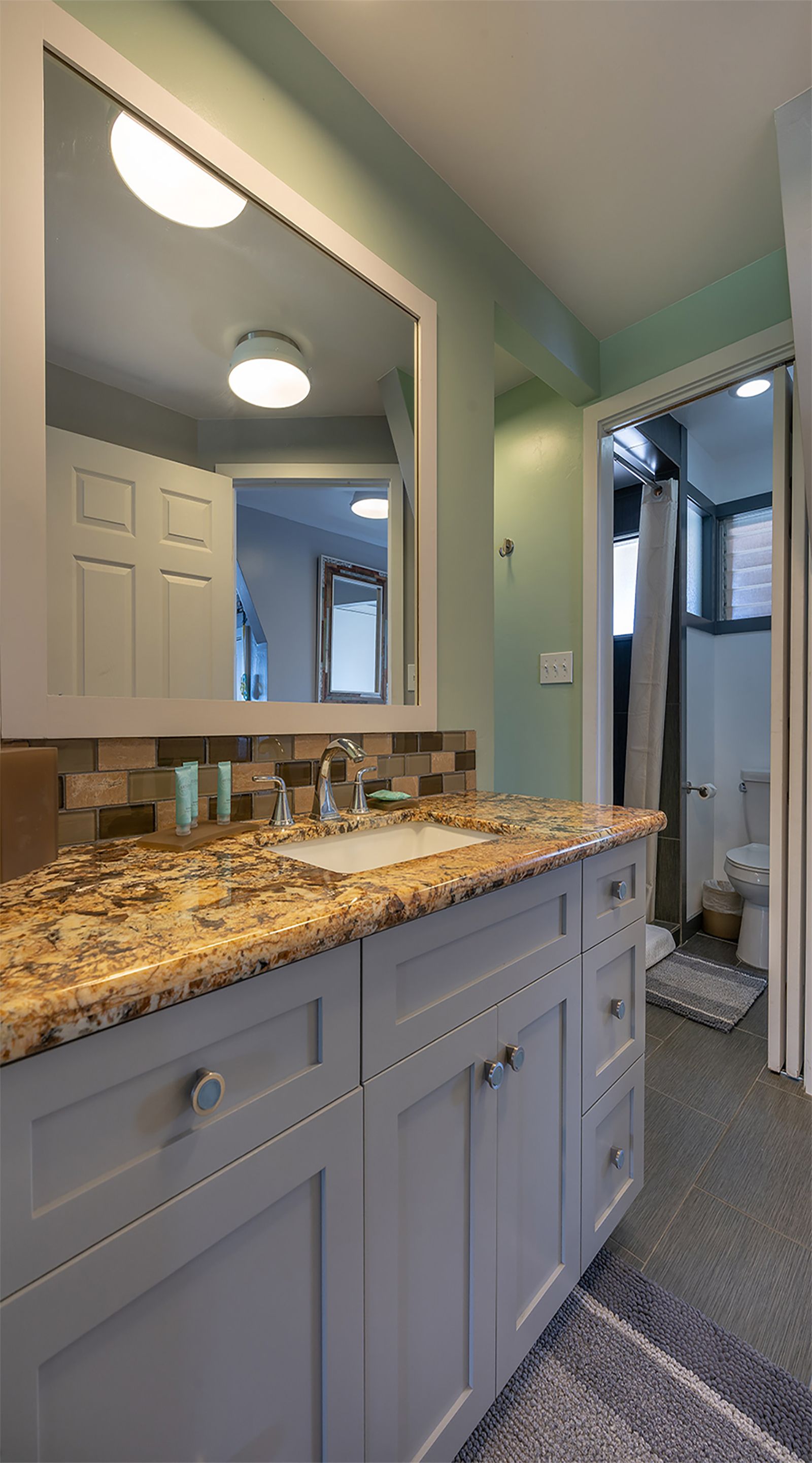 A bathroom with a granite countertop, a sink, a mirror, and a shower area.