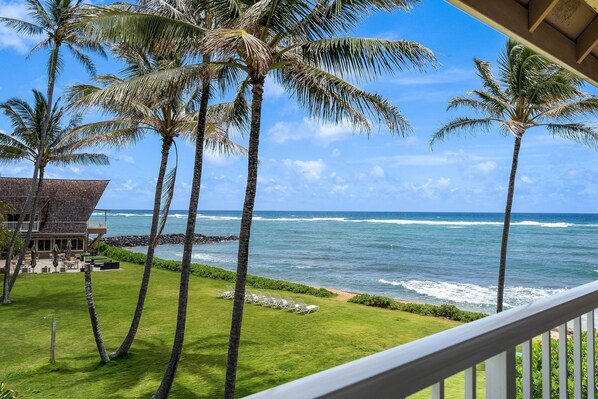 A view of the ocean from a balcony with palm trees and a building in the background.