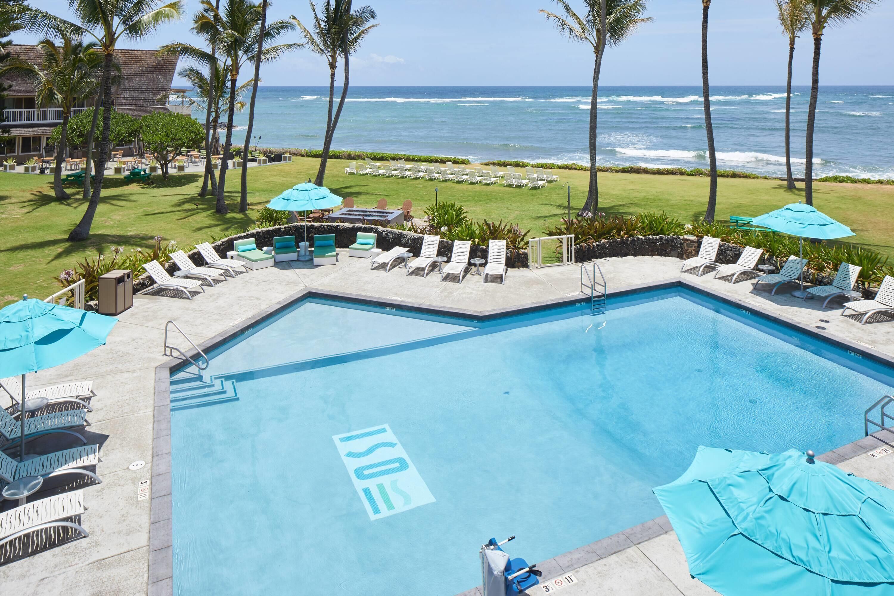 A pool area with lounge chairs and umbrellas, overlooking the ocean.