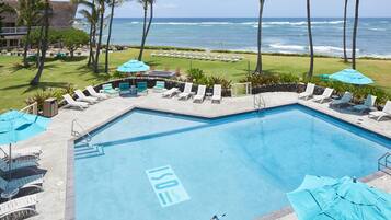 A pool area with lounge chairs and umbrellas, overlooking the ocean.