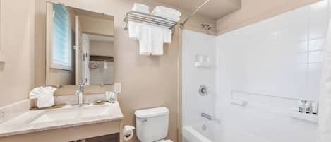 A modern bathroom with a sink, toilet, and bathtub. There is a towel rack above the toilet and a mirror above the sink.