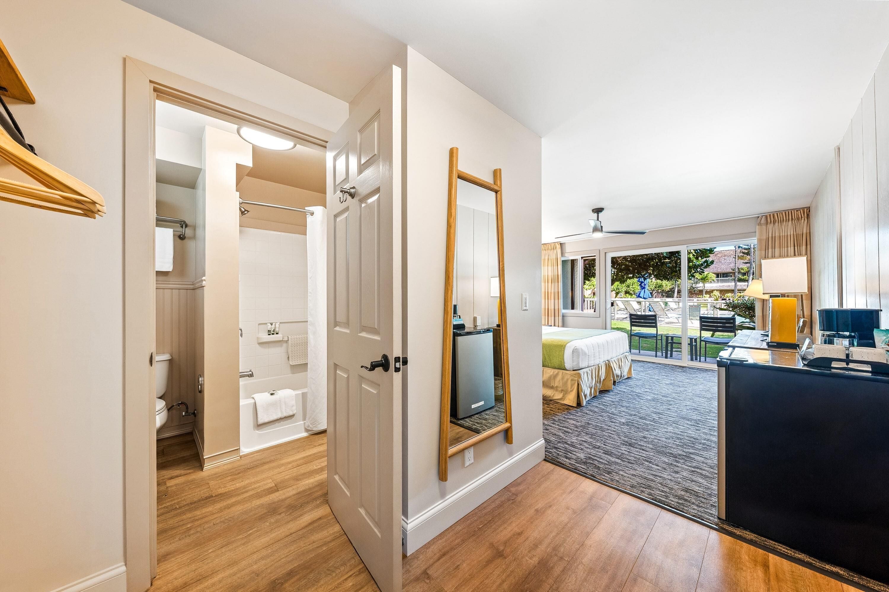 A hotel room with a wooden floor, a large mirror, a TV, and a view of the outdoor patio.