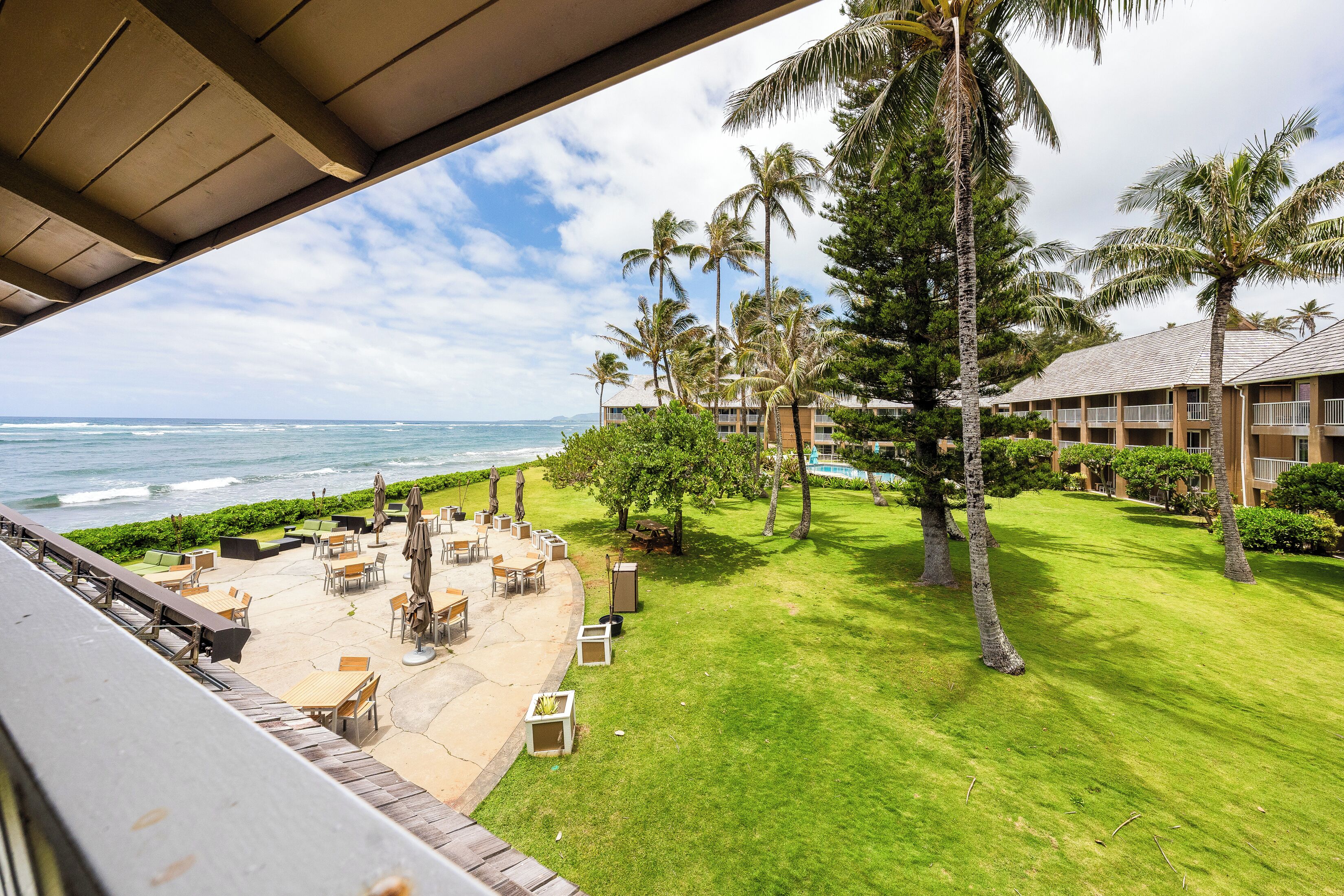 A view of a hotel with a pool area, outdoor seating, and a view of the ocean.