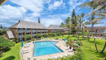 A hotel with a swimming pool surrounded by lounge chairs, palm trees, and a well-maintained lawn.