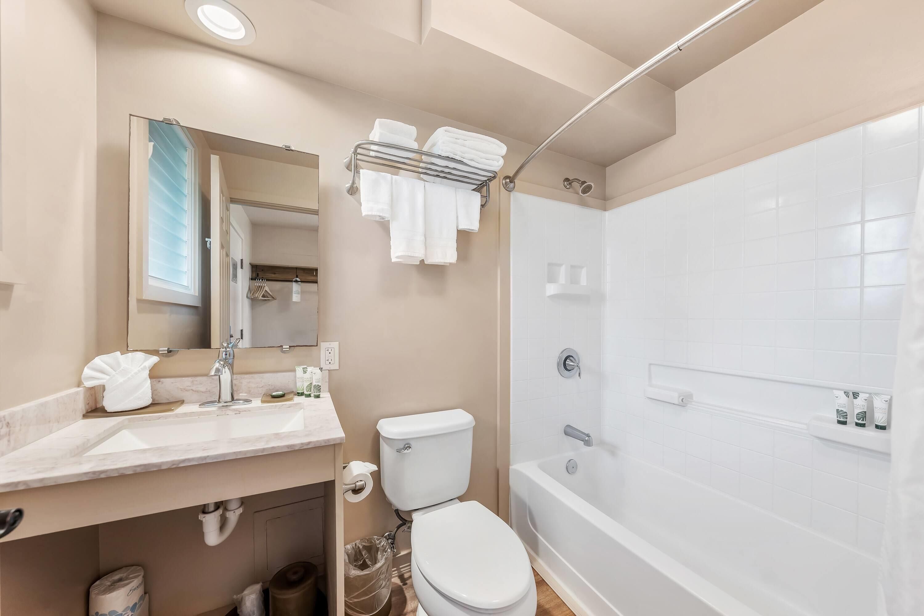 Un baño moderno con lavamanos, inodoro y ducha. Hay un toallero sobre el inodoro y un espejo sobre el lavamanos.