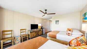 Habitación de hotel con dos camas, televisión, escritorio con lámpara y ventilador de techo.